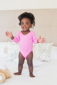 Baby girl in pink babygro standing on bed at home in the bedroom